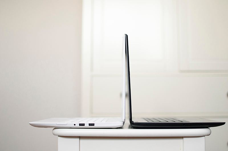 Two laptops, one white and one black, back to back on a small white table